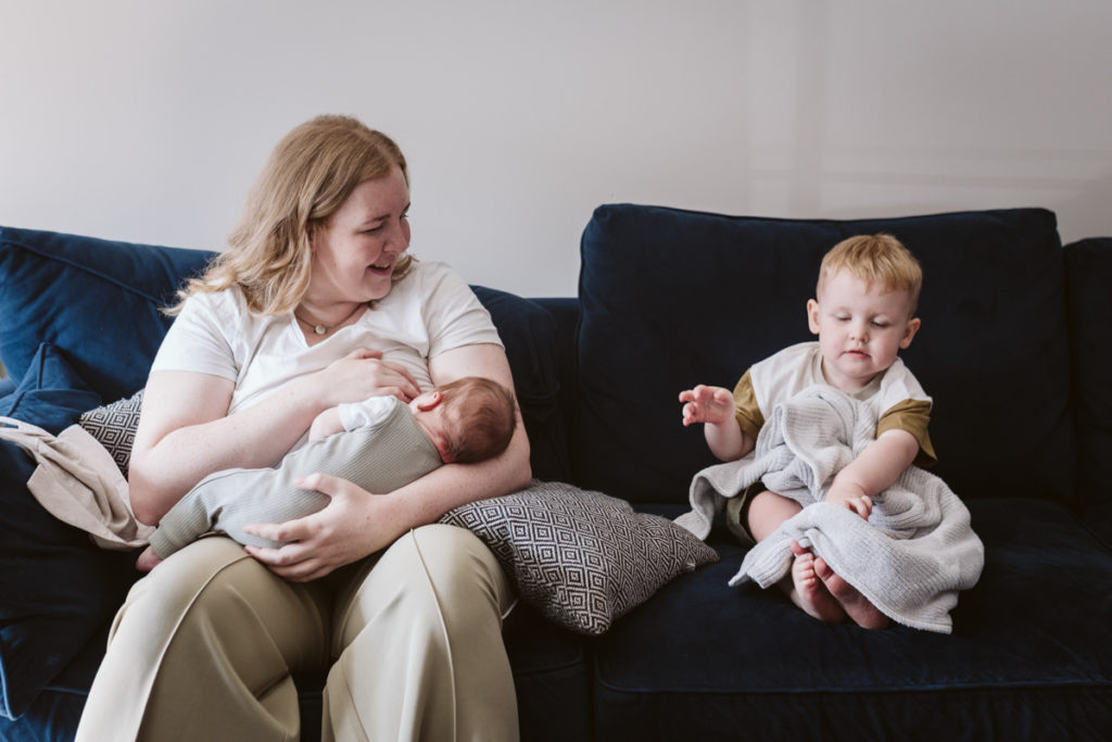 Toddler attempts to tuck himself in while Mum is busy feeding his baby brother