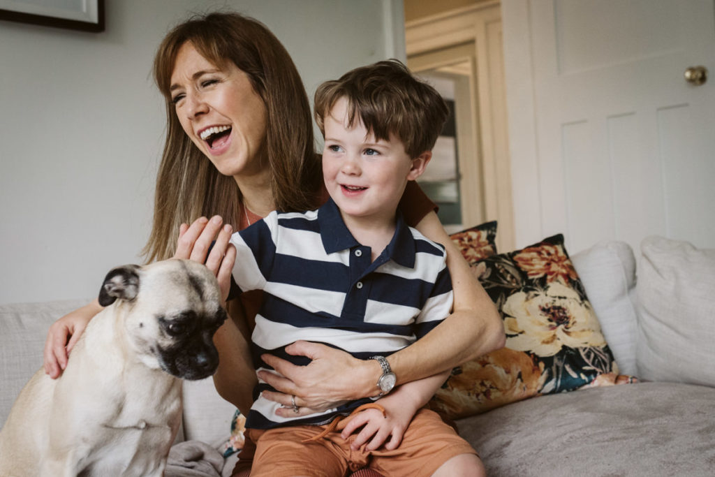Mum laughing naturally during a family photoshoot with her young son and dog.