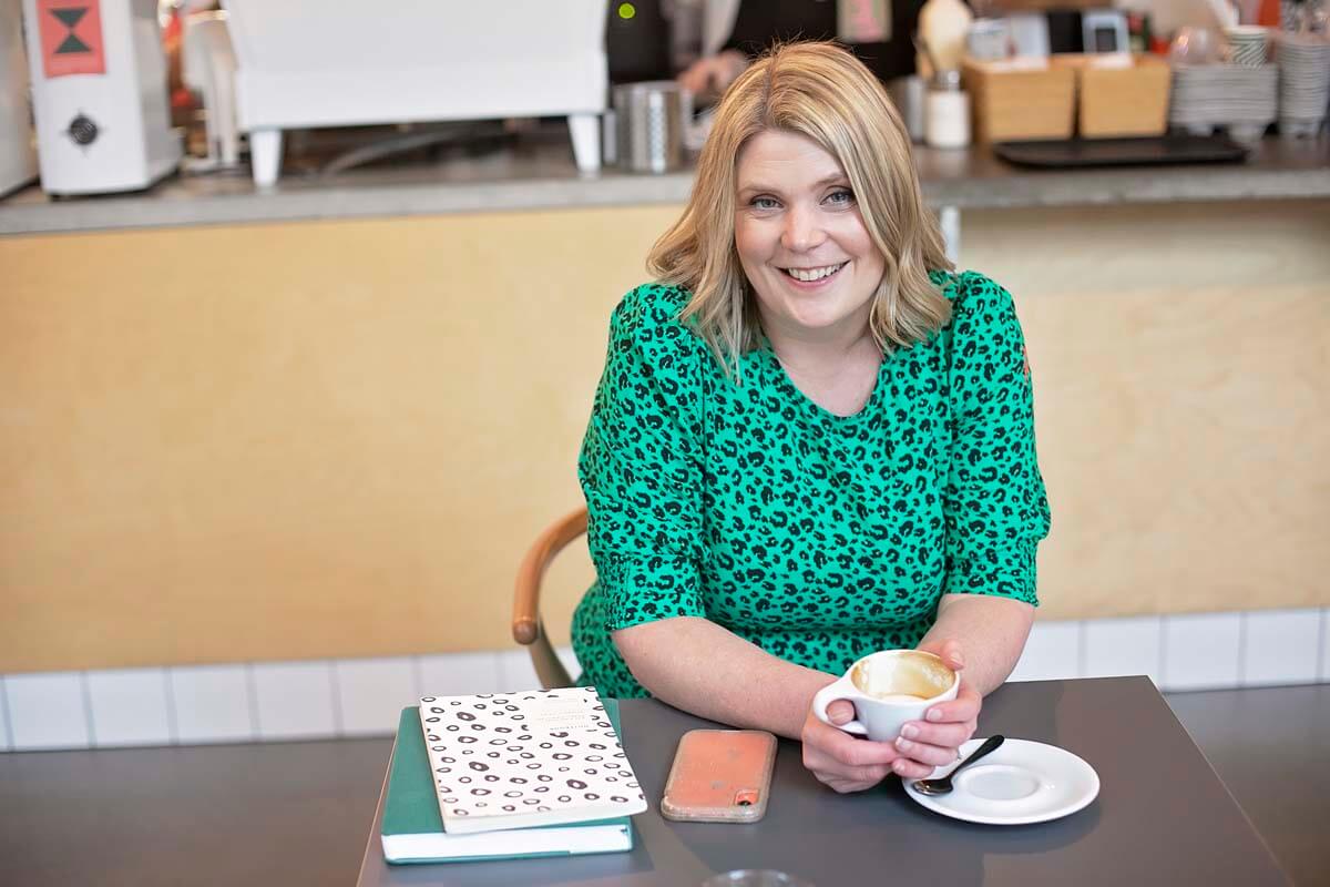 Hannah Brooke in a coffee shop wearing a green top and smiling