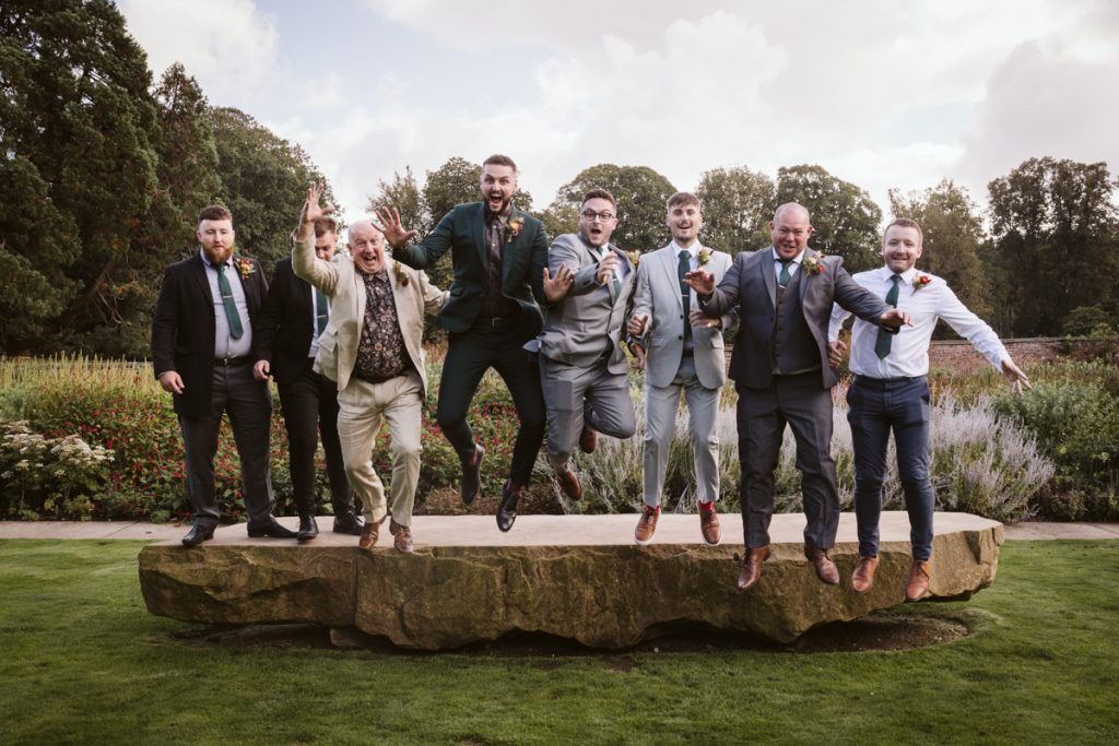 A fun group shot of the Groomsmen jumping off a rock in the Walled Garden of the Fig House, Middleton Lodge