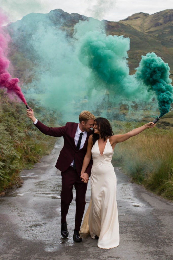 The bride and groom holding smokebombs against epic scenery in the Lake District