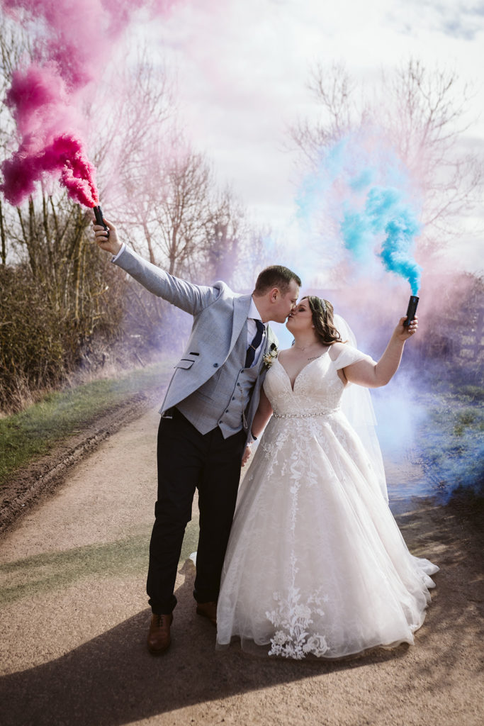 The newlyweds pose for a kiss with blue and pink smokebombs