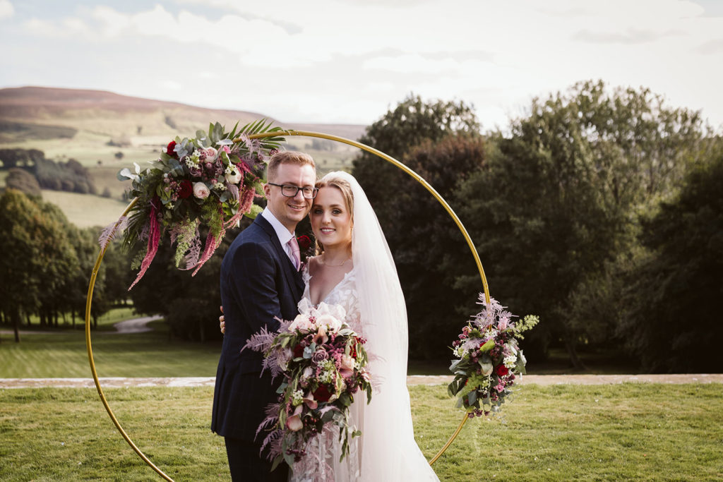 The Bride & Groom pose for a photo in front of their floral display and with the beautiful North Yorkshire countryside behind them.