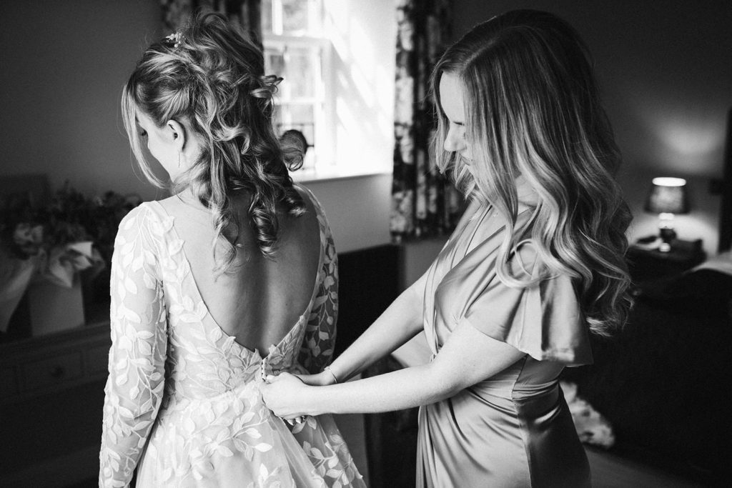 A bridesmaid helping the bride into her stunning Madi Lane Bridal dress