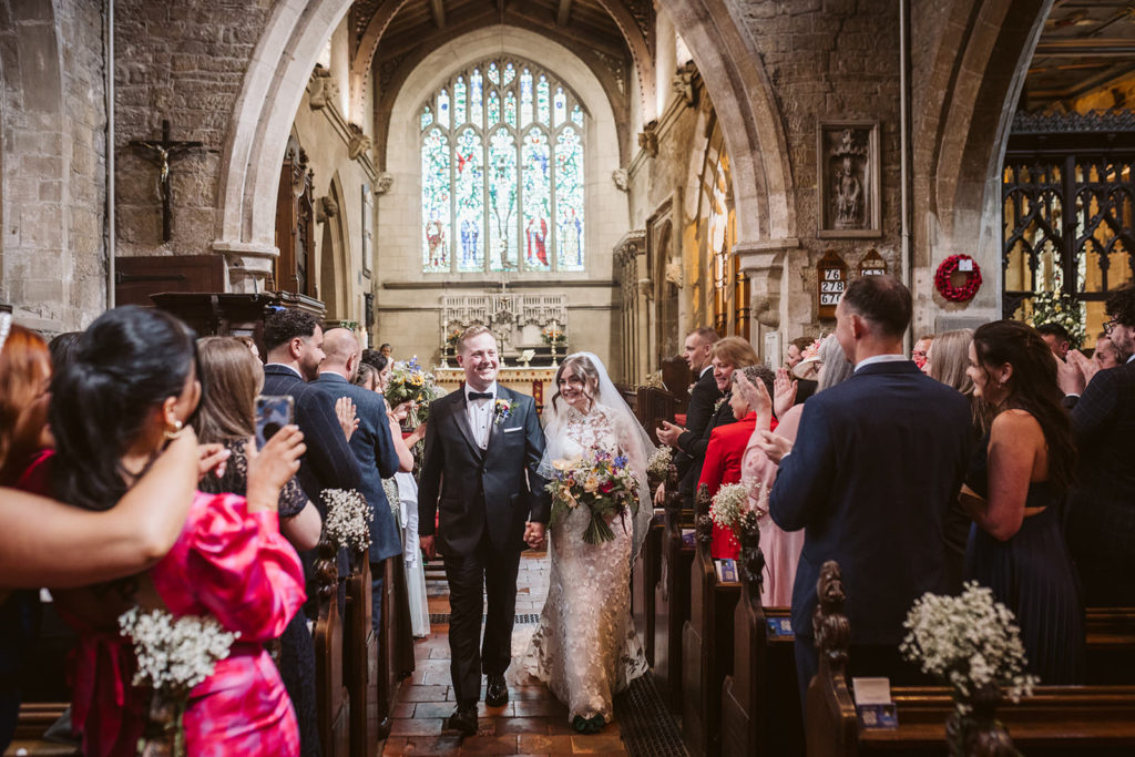 The newlywed couple smile at guests as they exit the church