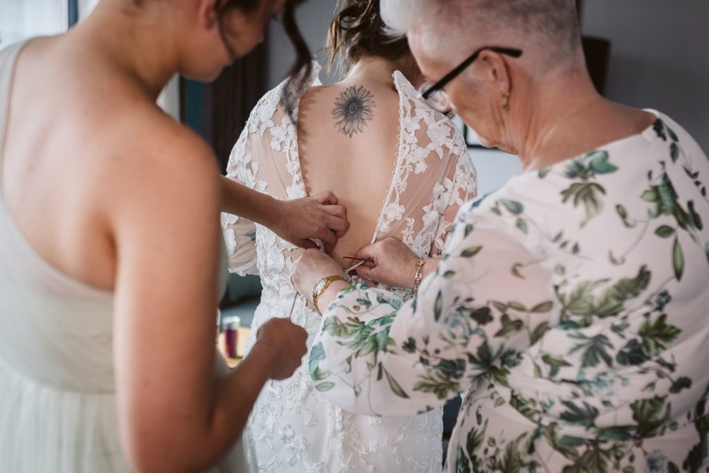 Bridesmaid and mother of the bride help the bride into her dress