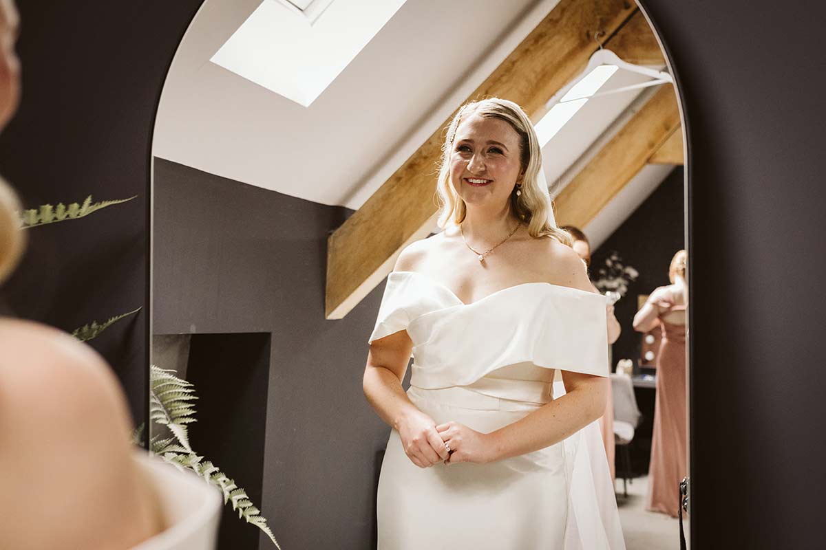 A bride looks at her reflection in the mirror while getting ready for her wedding at Oakwood at Ryther