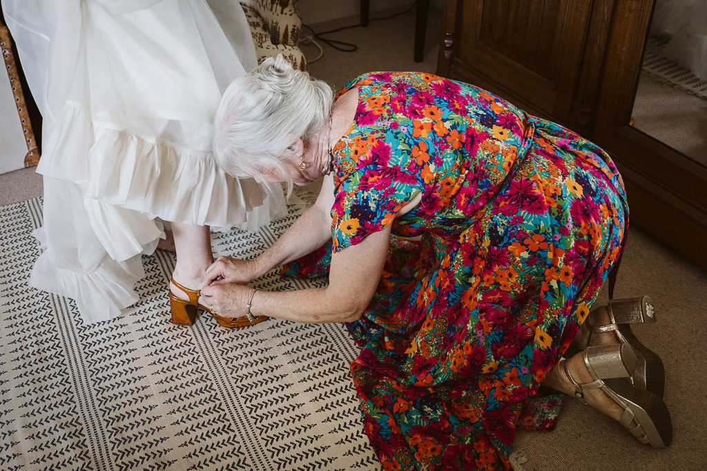 The mother of the bride on her hands and knees fastening the bride's shoe